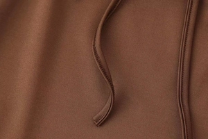 Detailaufnahme des braunen Strickbodys mit Spitzenpatchwork und passenden Kordelzügen