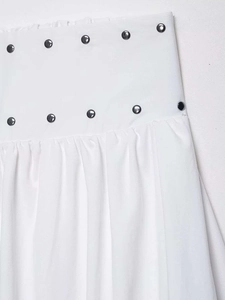 Detailed view of the white midi skirt featuring dual rows of metallic rivet studs at the waist