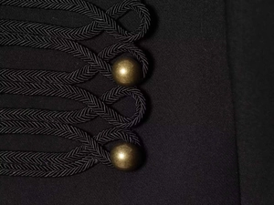 Détail de fermeture à cordon tressé noir et boutons en métal bronze mat sur veste chic
