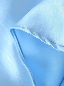 Détail de l'ourlet de la robe en satin bleu clair montrant la texture soyeuse et la couture