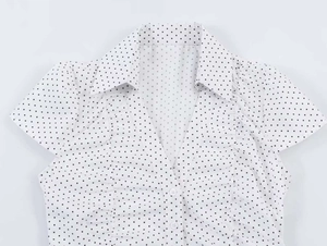 Close-up of white V-neck blouse with black polka dots and ruffle detail on placket