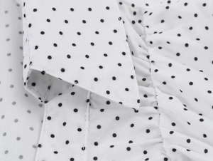 Detail view of V-neckline with ruffle trim on a retro white polka dot short sleeve shirt