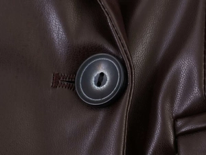 Macro detail of the black button and precision stitching on the brown PU leather blazer