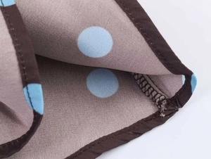 Close-up of brown chiffon dress fabric featuring light blue polka dots and neat hem stitching