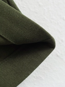 Detailed close-up of dark green ribbed knit fabric texture on a fashion jacket sleeve