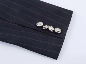 Detail of grey pinstripe blazer sleeve featuring four decorative silver metal buttons