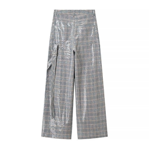 Detail view of grey plaid trousers with metallic sequins and long decorative ribbon