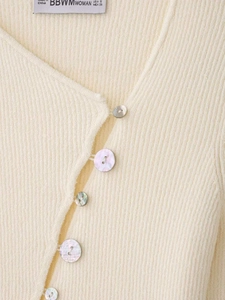 Détail d'un cardigan en maille côtelée beige avec col en V et boutons nacrés
