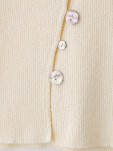 Détail d'un cardigan en maille côtelée avec boutons en nacre sur tissu crème doux