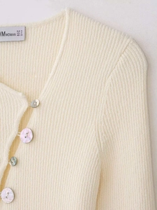 Détails de la maille côtelée et des boutons nacrés sur ce cardigan en tricot blanc cassé