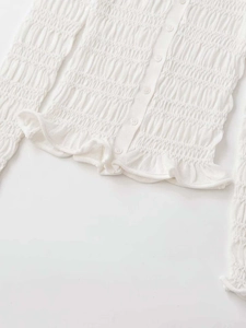 Close-up of white knitted cardigan featuring smocked texture and ruffle hem details