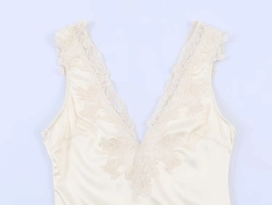 Dettaglio del body smanicato crema con scollo a V in pizzo e trama in raso lucido