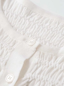 Close-up of white pleated knit cardigan featuring round buttons and ribbed neckline detail