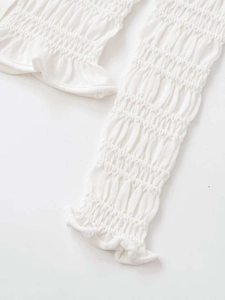 Close-up detail of white knitted cardigan featuring smocked texture and ruffle edge finish