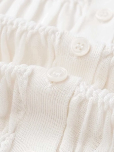 Detailed macro view of white knitted cardigan showing vertical texture and buttons
