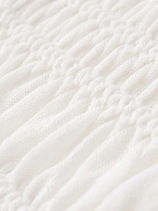 Detailed macro view of white smocked fabric texture and pleated knitted cardigan material