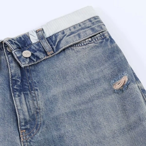 Detail of high waist ripped jeans with elastic waistband and silver button closure
