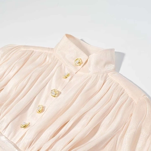 Gros plan sur le tissu en satin plissé avec boutons fleur dorée et perle de la robe rose