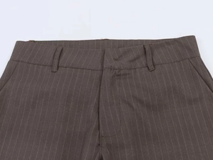 Detail of loose-fit brown striped trousers showing waistband and side pocket texture