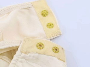 Dettaglio dei bottoni automatici gialli su tessuto in pizzo e raso beige