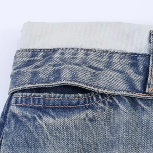 Macro view of blue denim jeans featuring a unique double-layered waistband and ripped edges