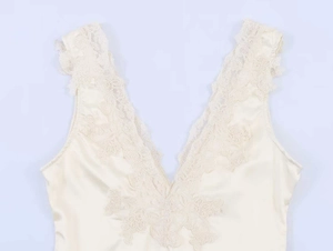 Dettaglio del body in raso crema con bordo in pizzo floreale e scollo a V profondo
