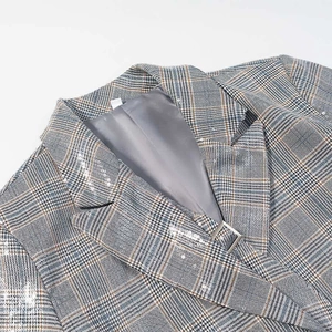 Detailed view of grey plaid blazer with silver sequins and a metal buckle on the lapel