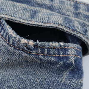 Macro detail of high-waisted distressed denim jeans showing frayed edges and orange stitching