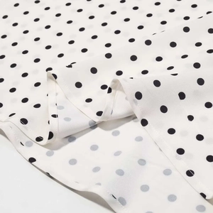 Vue détaillée du tissu en mousseline blanche à pois noirs et ourlet aux points fins