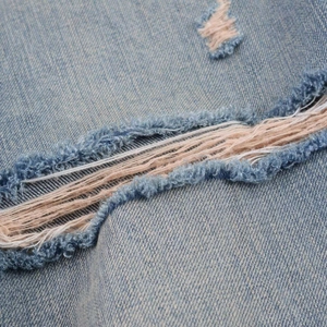 Detailed macro view of light blue distressed denim with frayed holes and washed texture