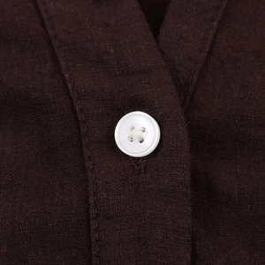 Detailed close-up of a white four-hole button on dark brown linen textured fabric