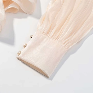 Détail d'une manche en satin plissé avec boutons en perles et base dorée couleur champagne