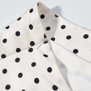 Détail de la fermeture éclair invisible et du motif à pois noirs sur tissu blanc