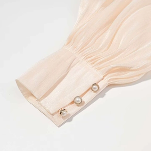 Détail des poignets plissés couleur champagne avec trois boutons en perle et bord doré