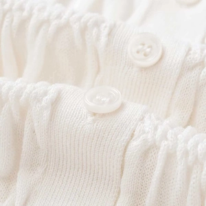 Minimalist white pleated knitted cardigan with close-up detail of buttons and texture