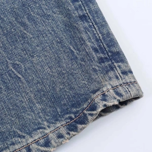 Detail view of washed blue denim fabric with floral pattern and orange contrast stitching