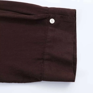 Close-up of loose-fit shirt cuff in dark coffee fabric with white button detail