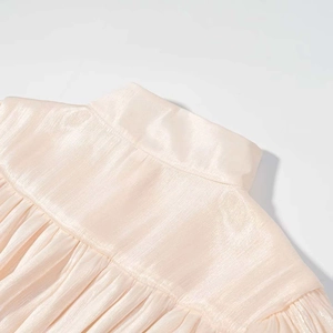 Détail du tissu satiné plissé champagne sur une robe à manches longues et col montant