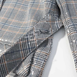 Detail of plaid blazer fabric featuring shimmering sequins and a fabric-covered button