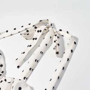 Détail des bretelles nouées ajustables sur une robe d'été blanche à pois noirs
