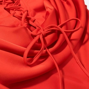 Detailed close-up of a red dress featuring criss-cross lacing and a delicate bow tie