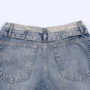 Detailed close-up of rear pockets and belt loops on high-waist distressed blue denim jeans