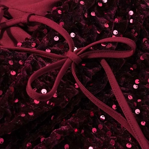 Détail macro du tissu à paillettes rouge vin avec un nœud en velours sur cette robe
