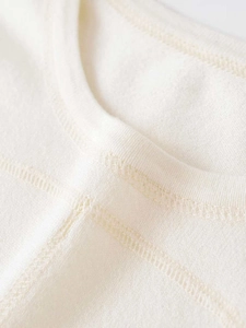 Detailopname van een ronde halslijn op een crèmekleurig gebreid shirt met nette stiksels