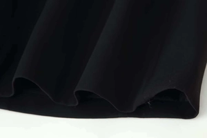 Vue détaillée de l'ourlet de la robe noire montrant la texture du tissu et le drapé ondulé