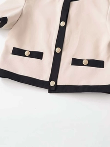 Gros plan du cardigan beige avec bordure noire et boutons dorés en relief élégants
