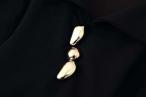 Close-up of three decorative gold liquid-metal buttons on black ruffled wide-leg jumpsuit