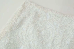 Detailed close-up of intricate ivory paisley lace fabric with refined edge stitching
