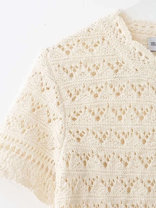 Close-up of beige short sleeve knit top showing intricate hollow crochet patterns and neck detail