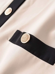 Détail de la bordure contrastée et des boutons dorés texturés sur le cardigan beige